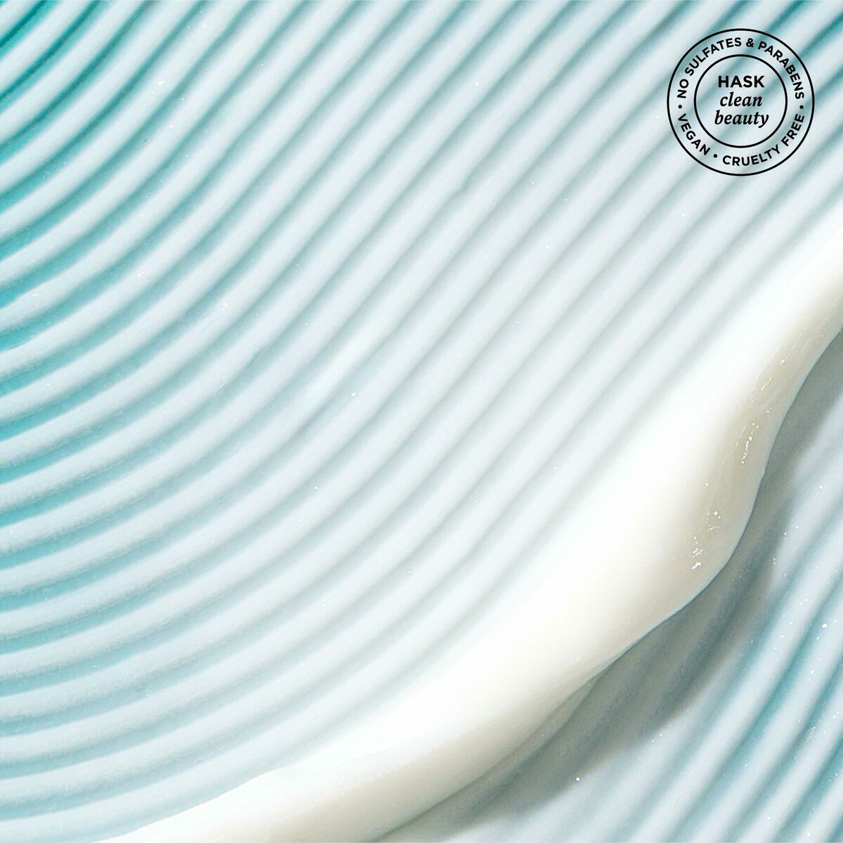 Masque réparateur HASK ARGAN OIL on a textured blue surface, showcasing its creamy texture and clean beauty credentials.