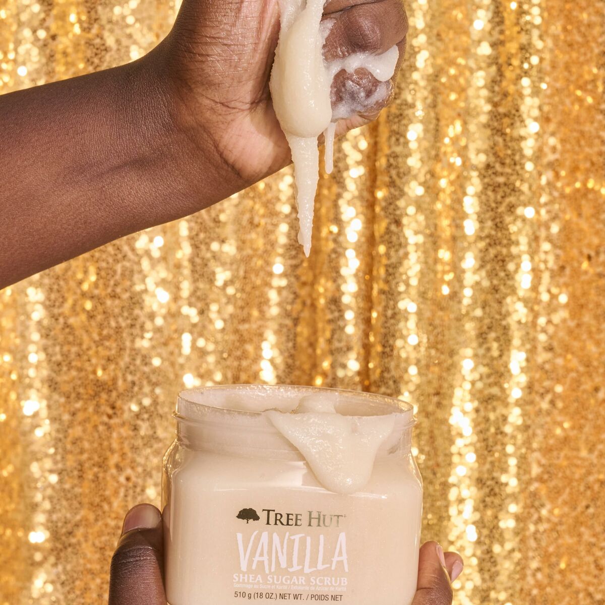 Close-up of hands holding Tree Hut Vanilla Shea Sugar Scrub, showcasing its creamy texture against a shimmering gold backdrop.