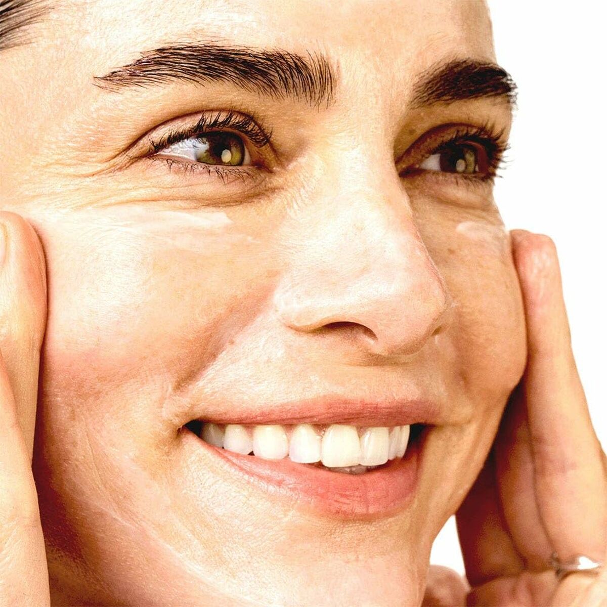 Femme souriante utilisant une crème hydratante pour le visage, mettant en valeur sa peau radieuse.