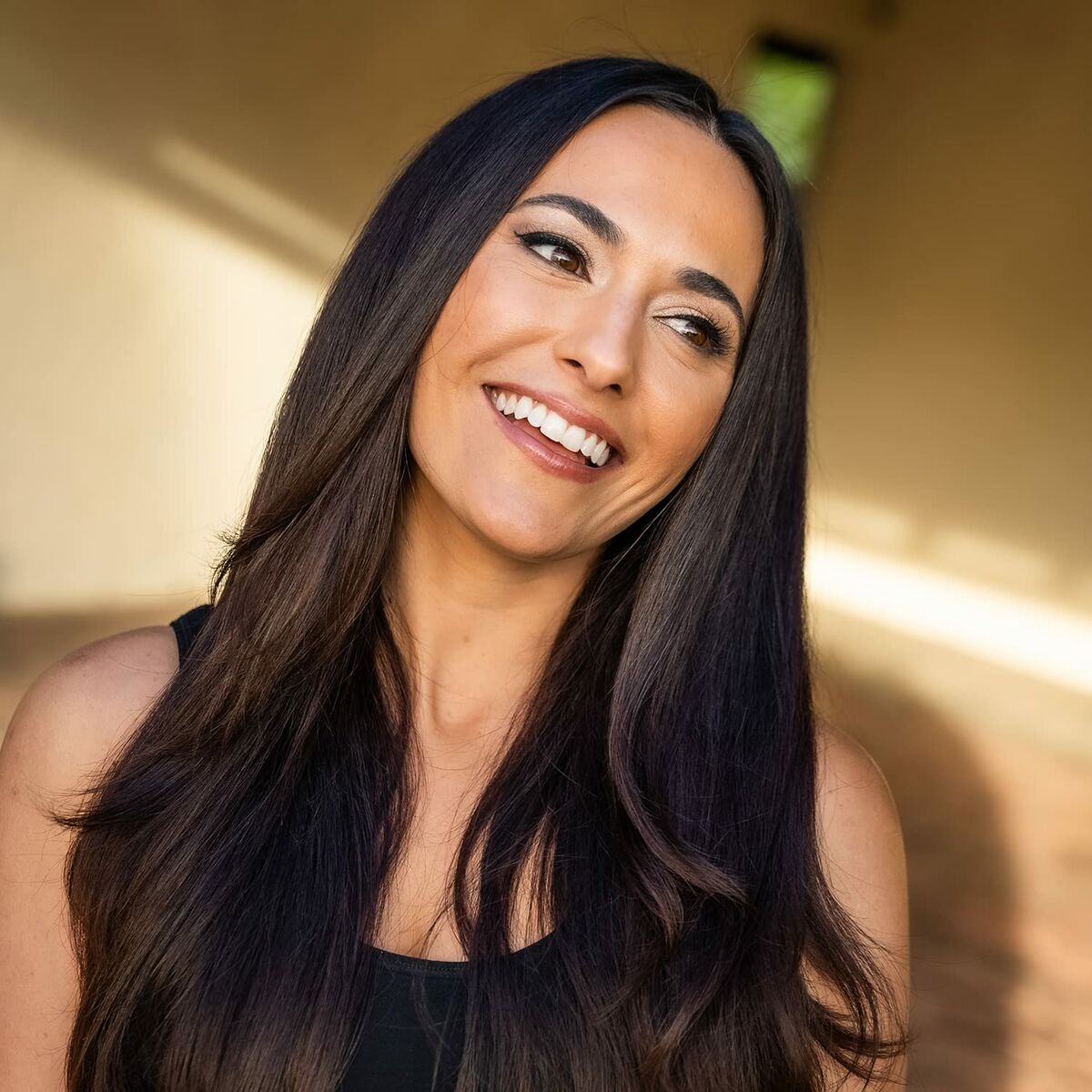 A woman with long, shiny hair smiling in a bright, natural setting.