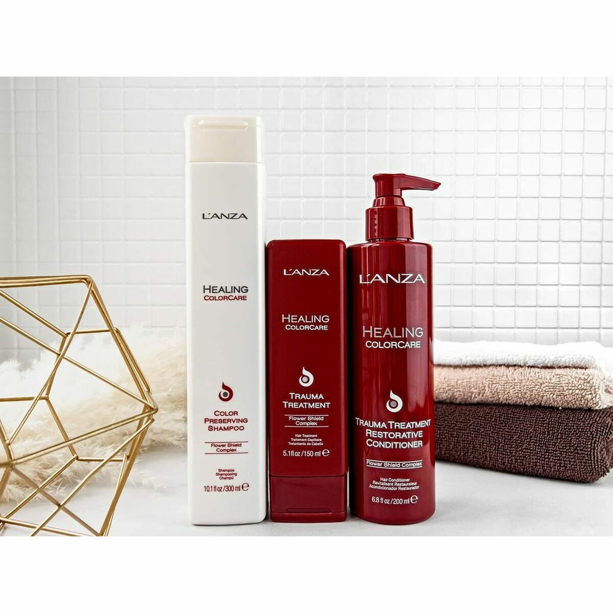 Set of L'ANZA Healing Colorcare shampoo, conditioner, and treatment on display with towels and a decorative basket.