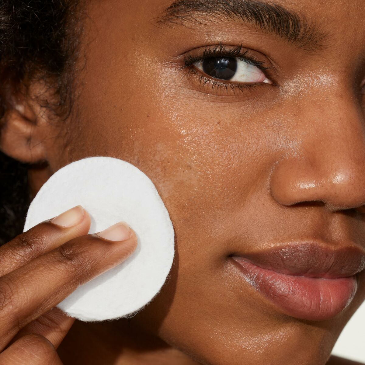 Model using Tonique exfoliant Origins YOUTHTOPIA 100 ml on her face with a cotton pad, promoting skin care routine.