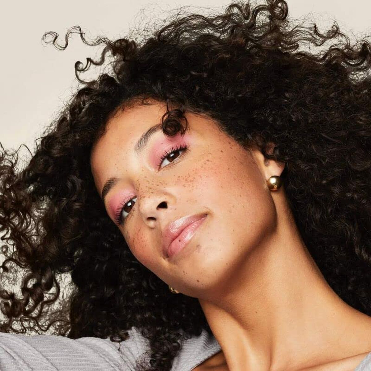 Woman with defined curly hair and pink eyeshadow showcasing Living Proof Curl product.