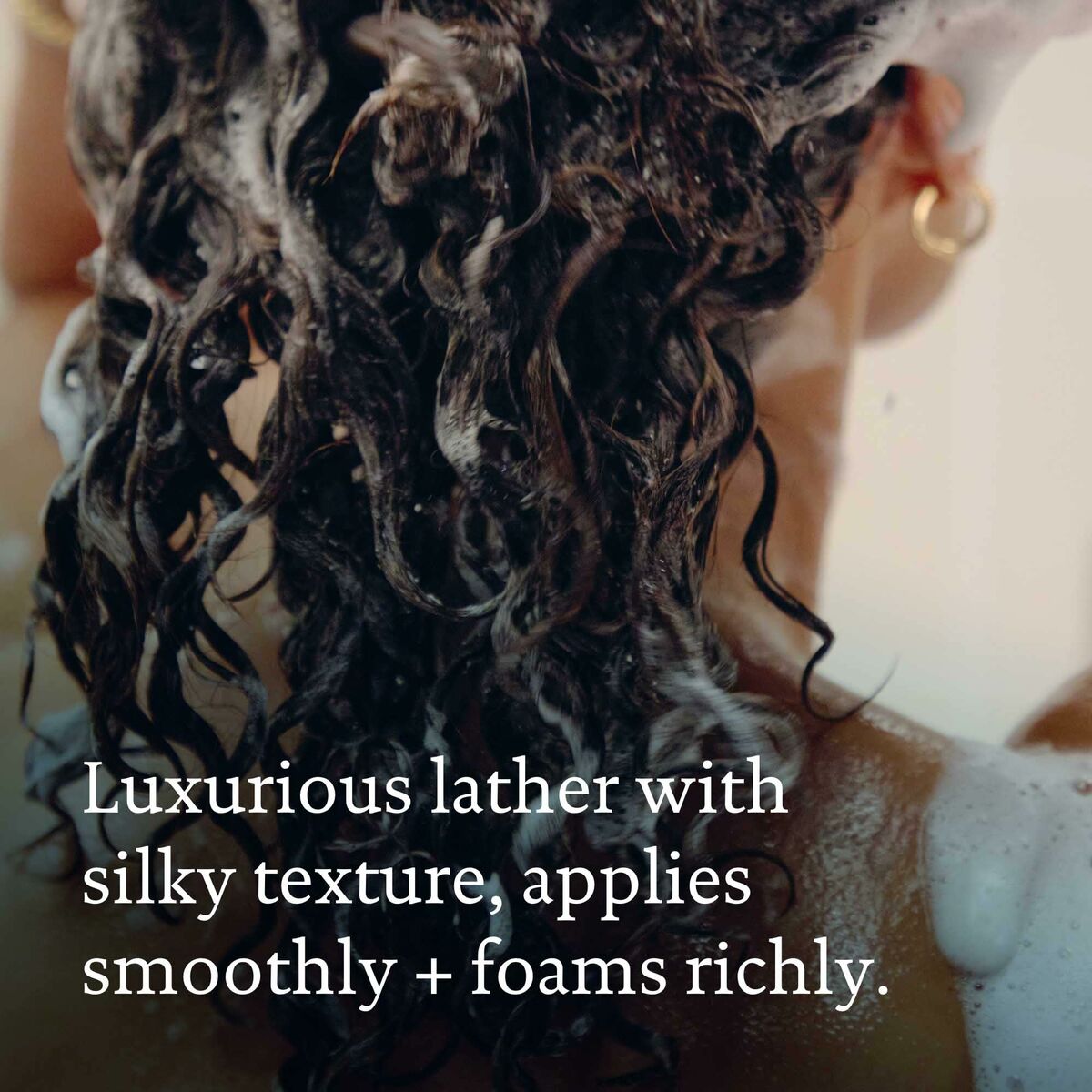 Person with curly hair applying shampoo, showcasing a luxurious lather and silky texture.