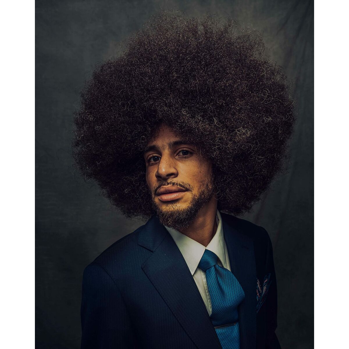 Portrait of a man in a suit with a large afro hairstyle against a dark background.