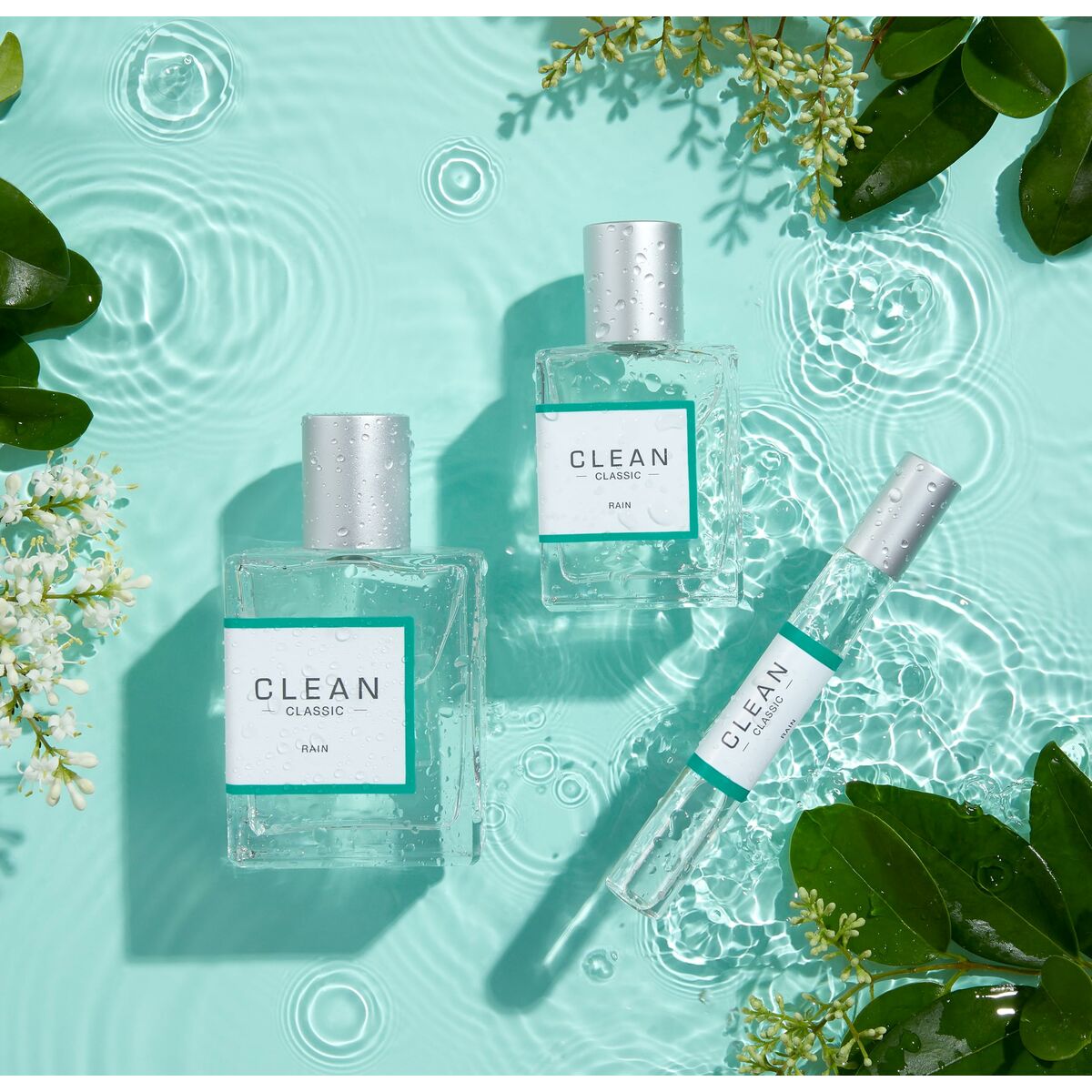 Bottles of Clean Classic fragrances including Rain displayed on a serene turquoise surface with greenery.