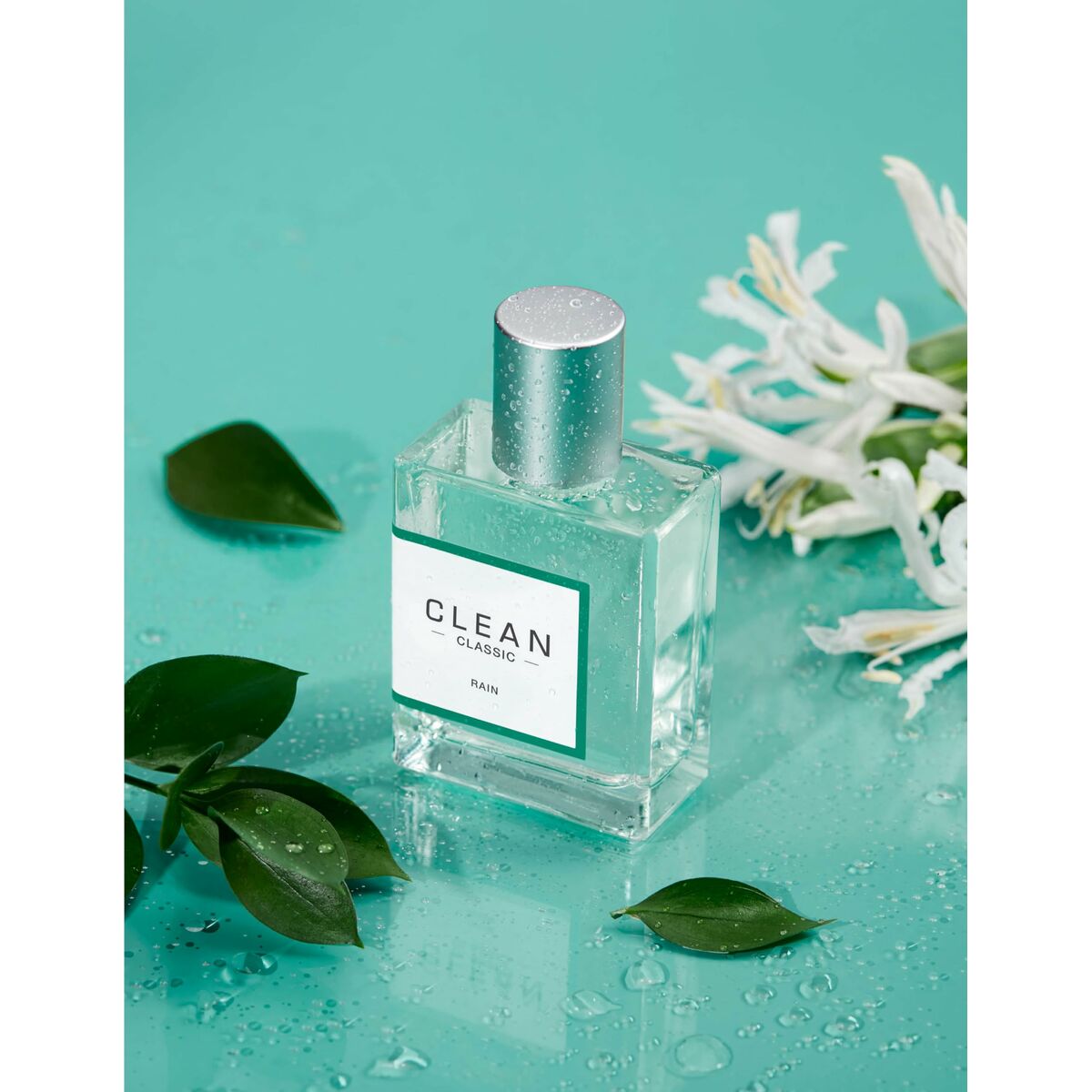 Clean Rain Eau de Parfum 60ml bottle surrounded by fresh leaves and flowers on a teal background.