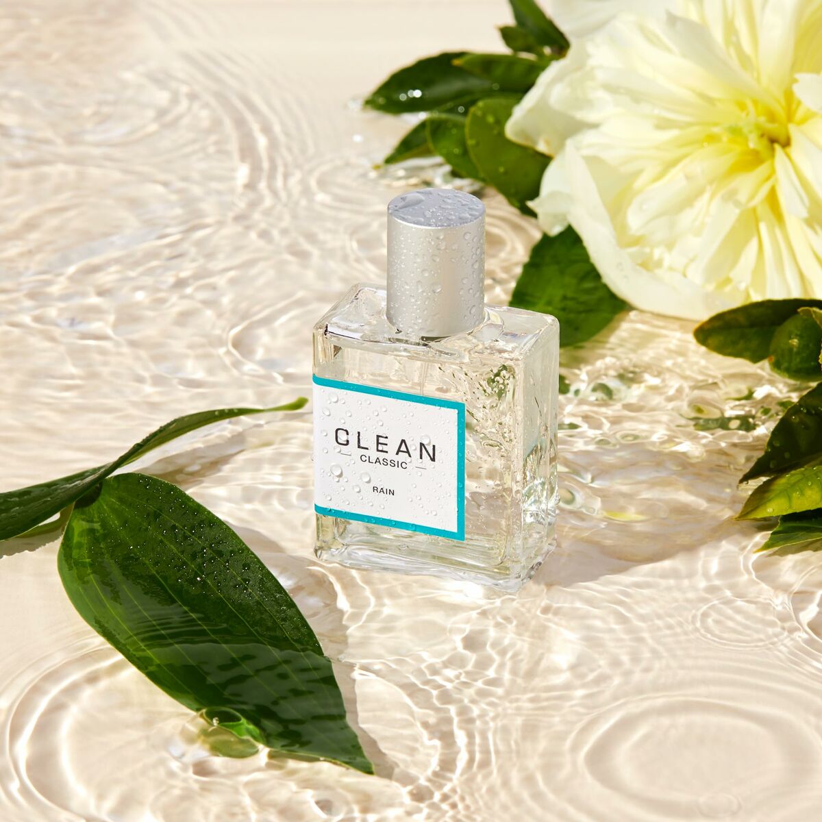 Bouteille de parfum Clean Classic Rain posée sur des feuilles et fleurs, capturant la fraîcheur de l'eau.
