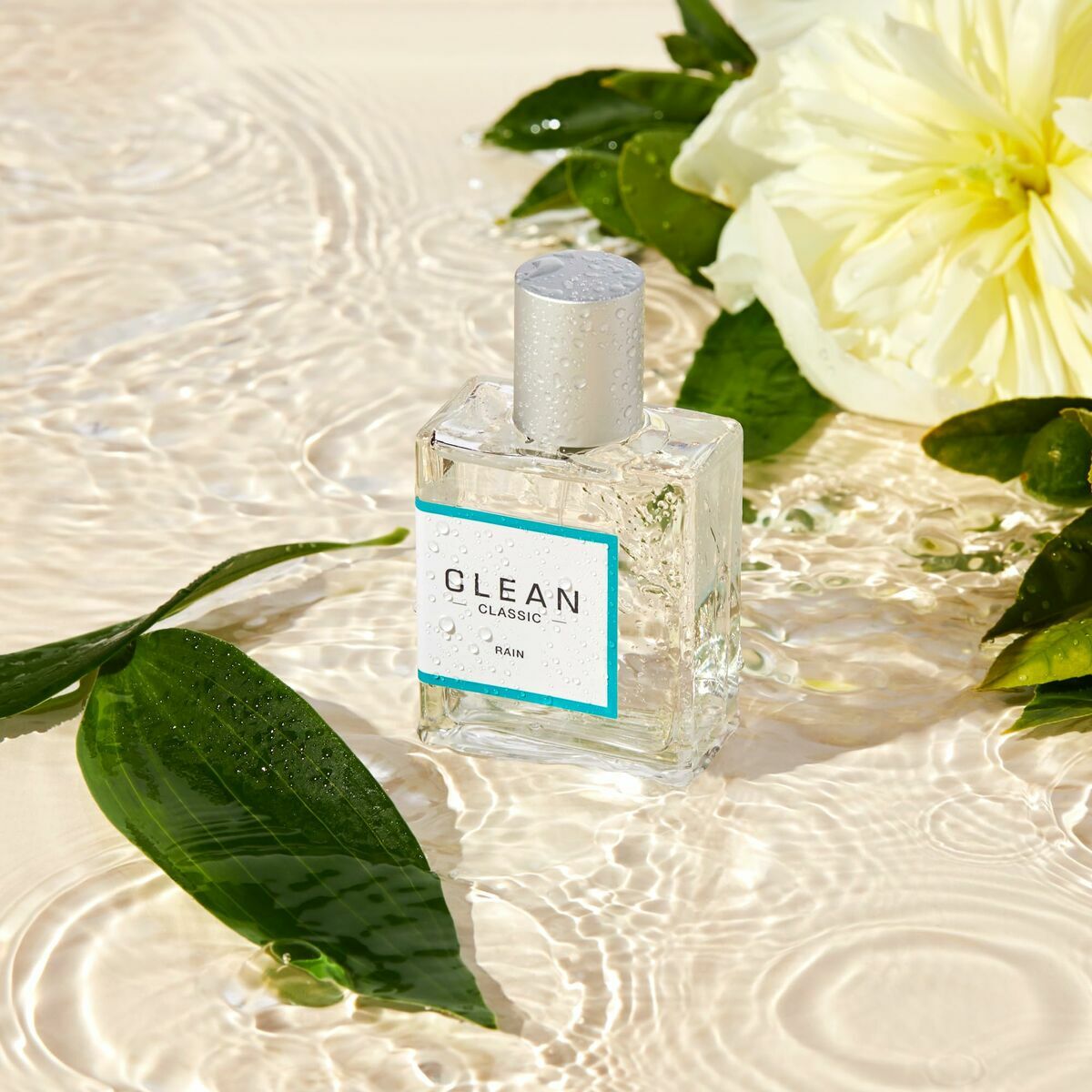 Parfum Femme Clean Rain EDP bottle lying on water with green leaves and a white flower.