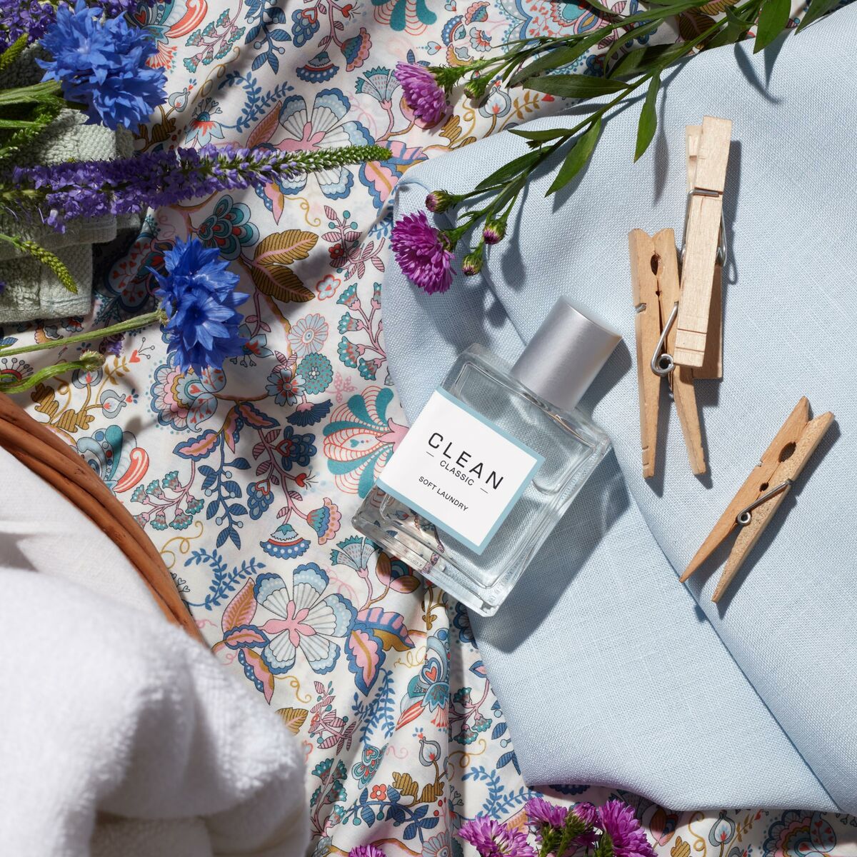 Bouteille de parfum unisexe Clean posée sur un tissu fleuri avec des fleurs et des pinces à linge.