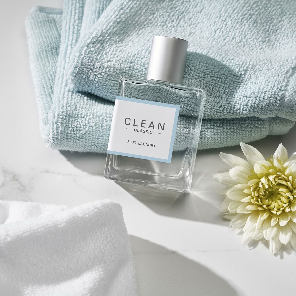 Parfum Clean Classic Soft Laundry sur une surface marbrée avec serviettes et une fleur