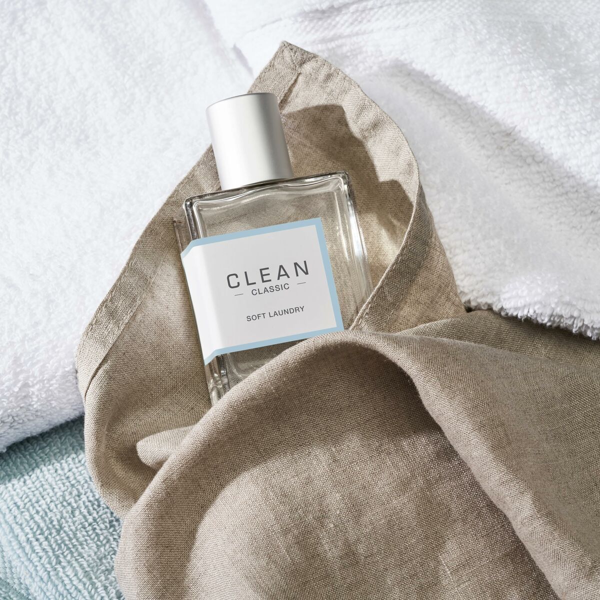 Bouteille de parfum Clean Classic Soft Laundry, posée sur du linge, évoquant une fragrance propre et fraîche.
