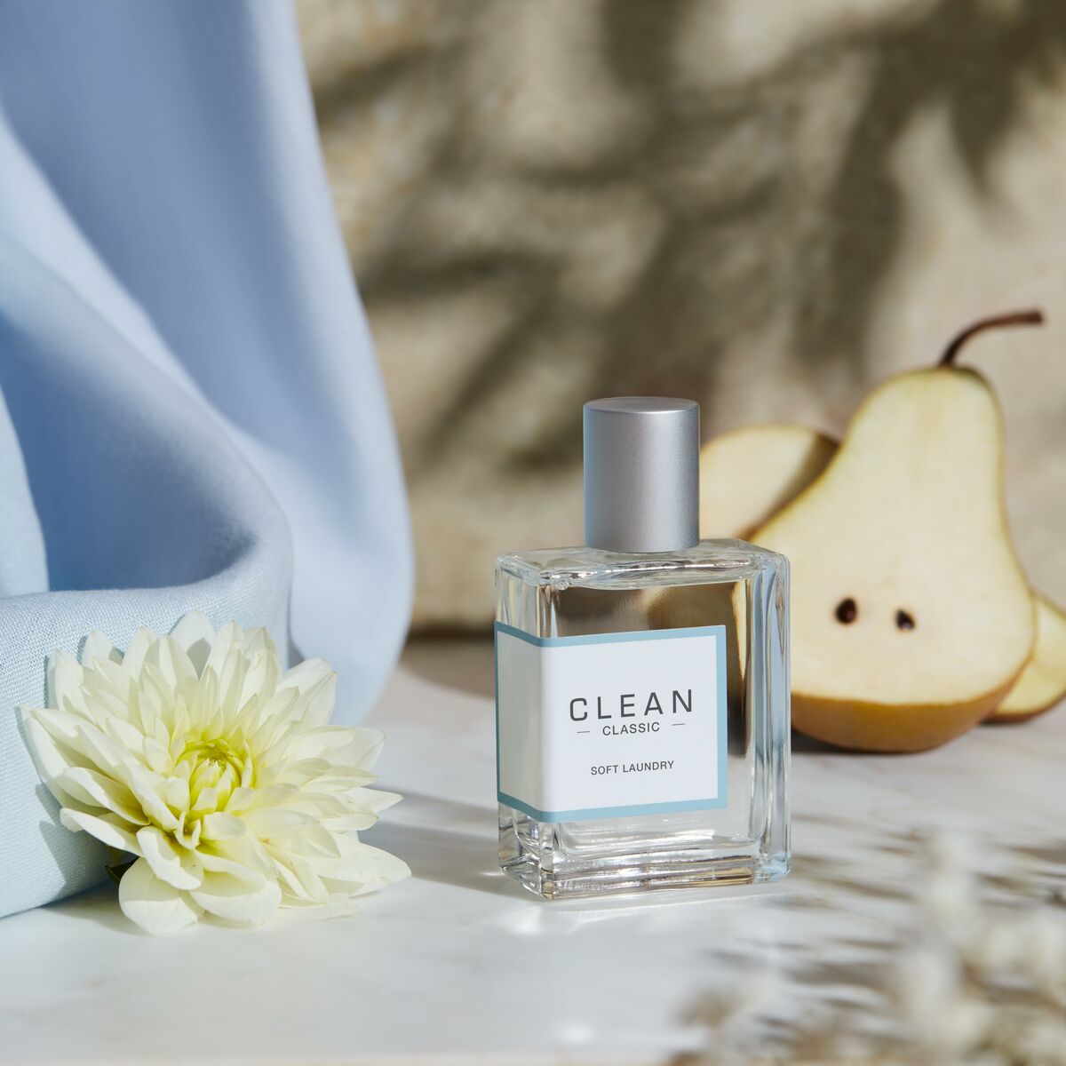 Parfum Unisexe Clean Soft Laundry, avec une fleur, une poire et un tissu bleu en arrière-plan.