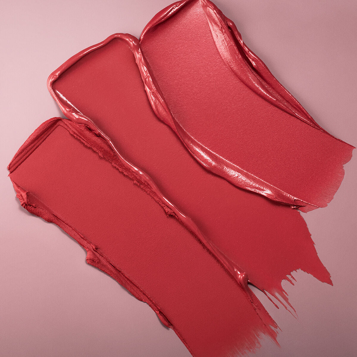 Swatches of Estee Lauder Pure Color Rebellious Rose lipstick on pink background, showcasing vibrant red shades.