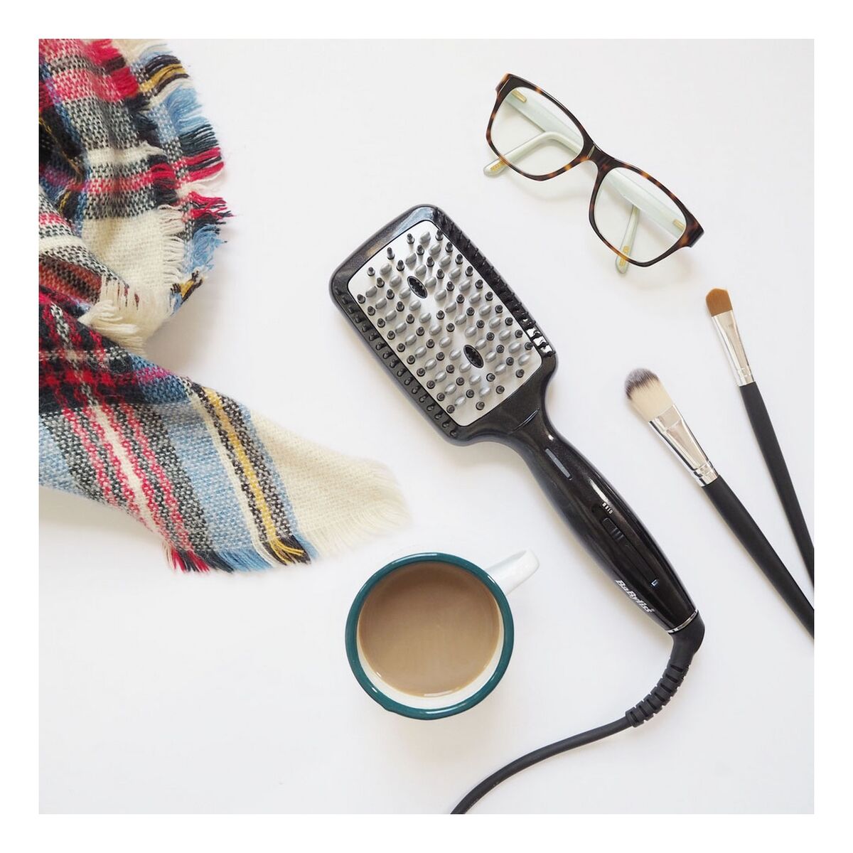 Brosse de lissage Babyliss HSB101E Céramique Noir avec accessoires, tasse et écharpe sur une table blanche.