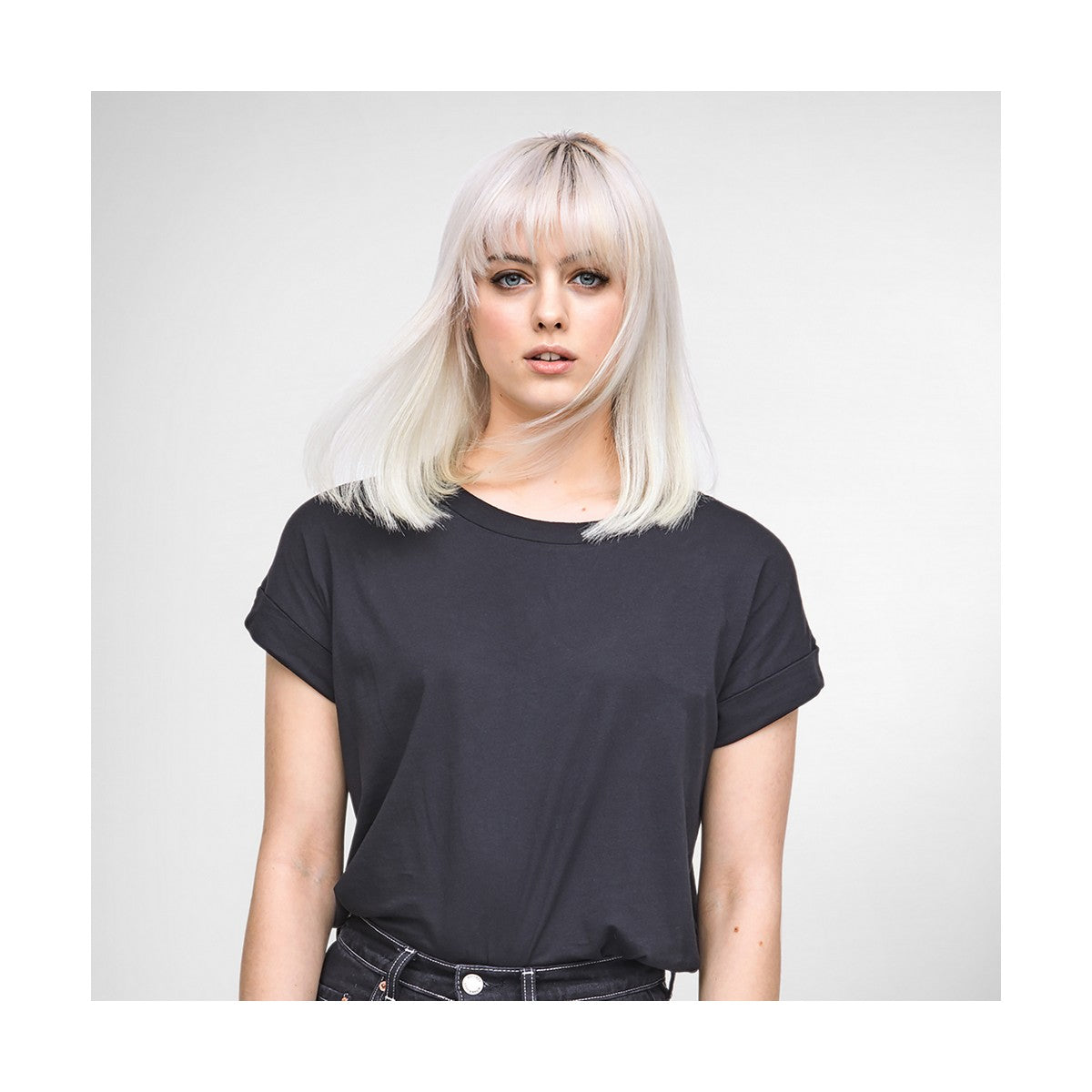 Femme avec cheveux blonds platine portant un t-shirt noir, posant avec un regard naturel.