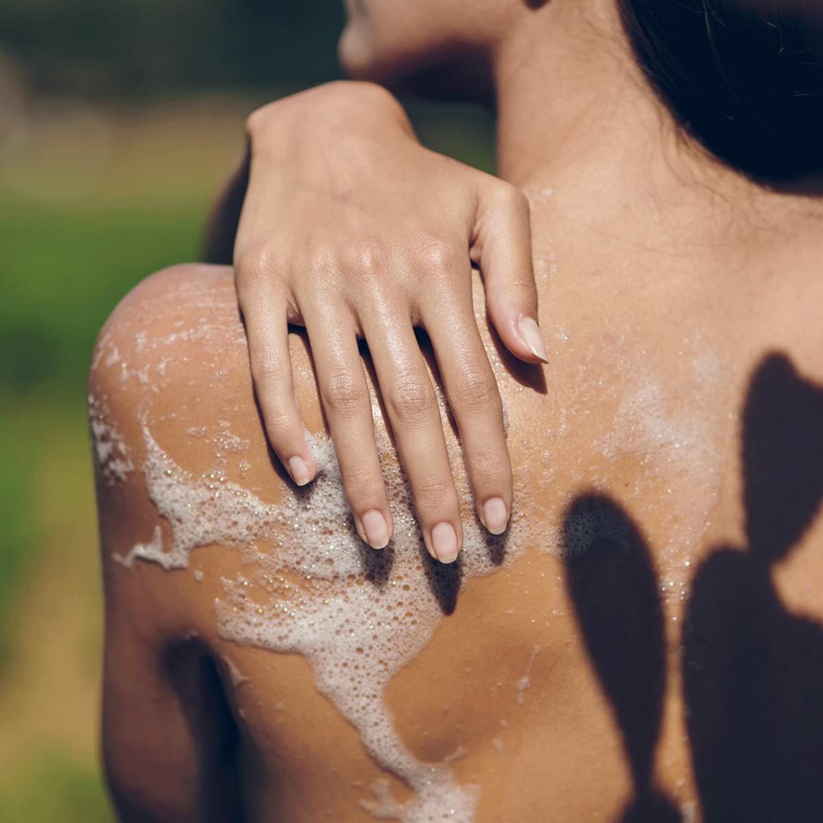 Close-up of a hand applying gel on a shoulder, showcasing a refreshing bath experience outdoors.