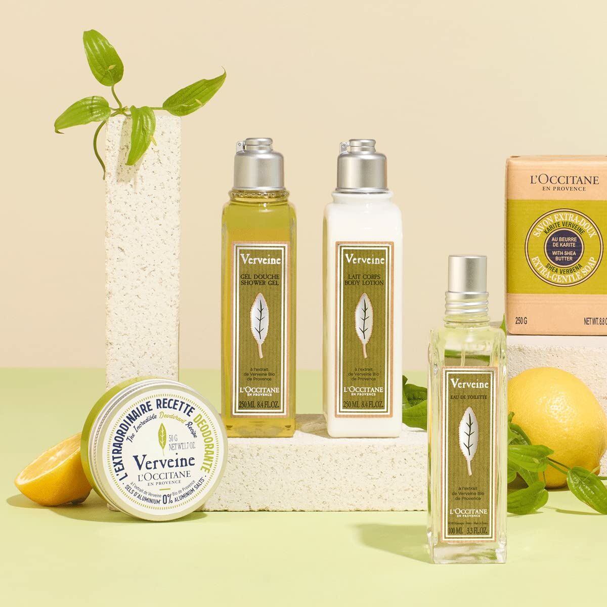 L'Occitane En Provence Verbena shower gel, body lotion, and fragrance on a pastel background, featuring natural ingredients.