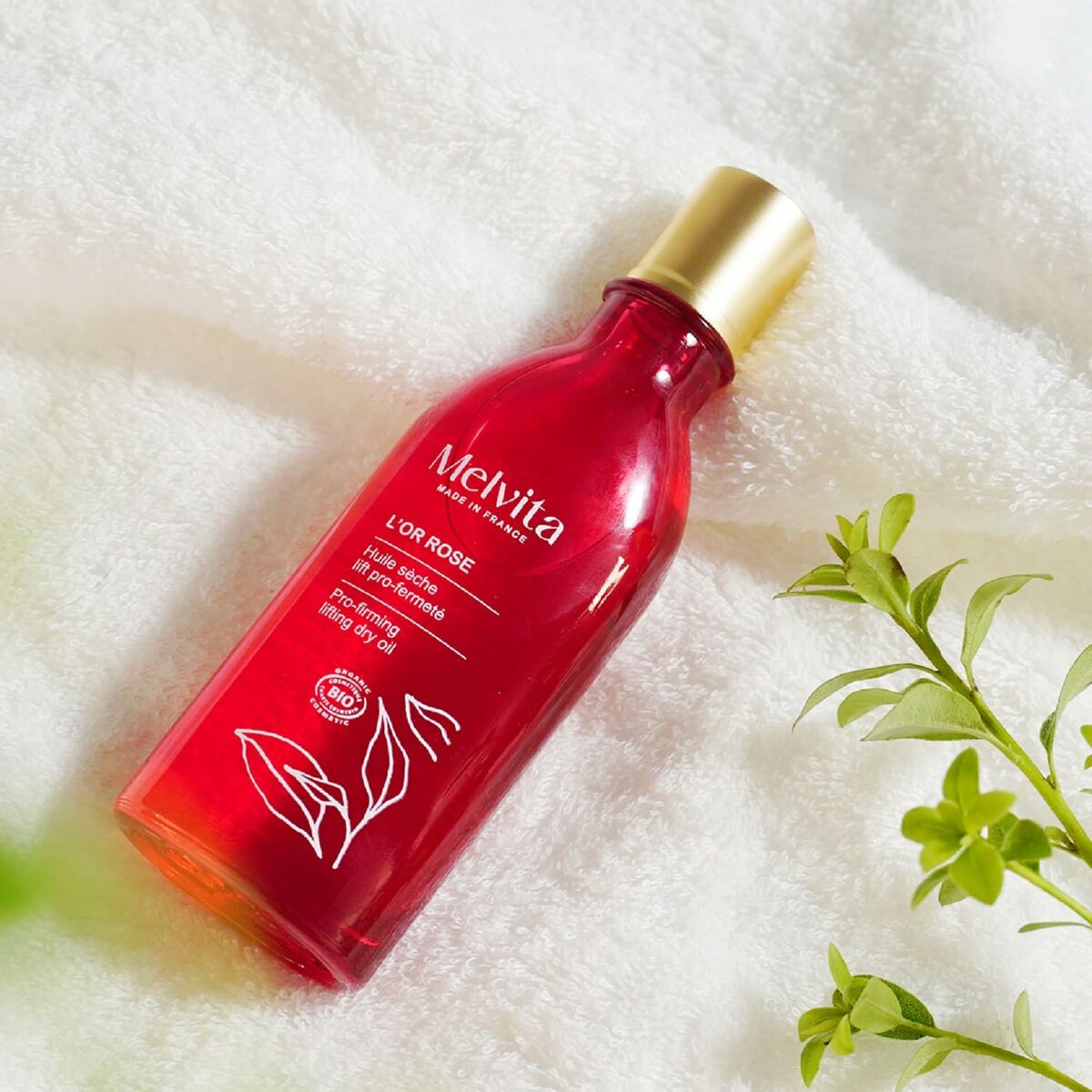 Lotion corporelle Melvita L'OR ROSE en bouteille rouge sur tissu doux, idéal pour l'hydratation de la peau.