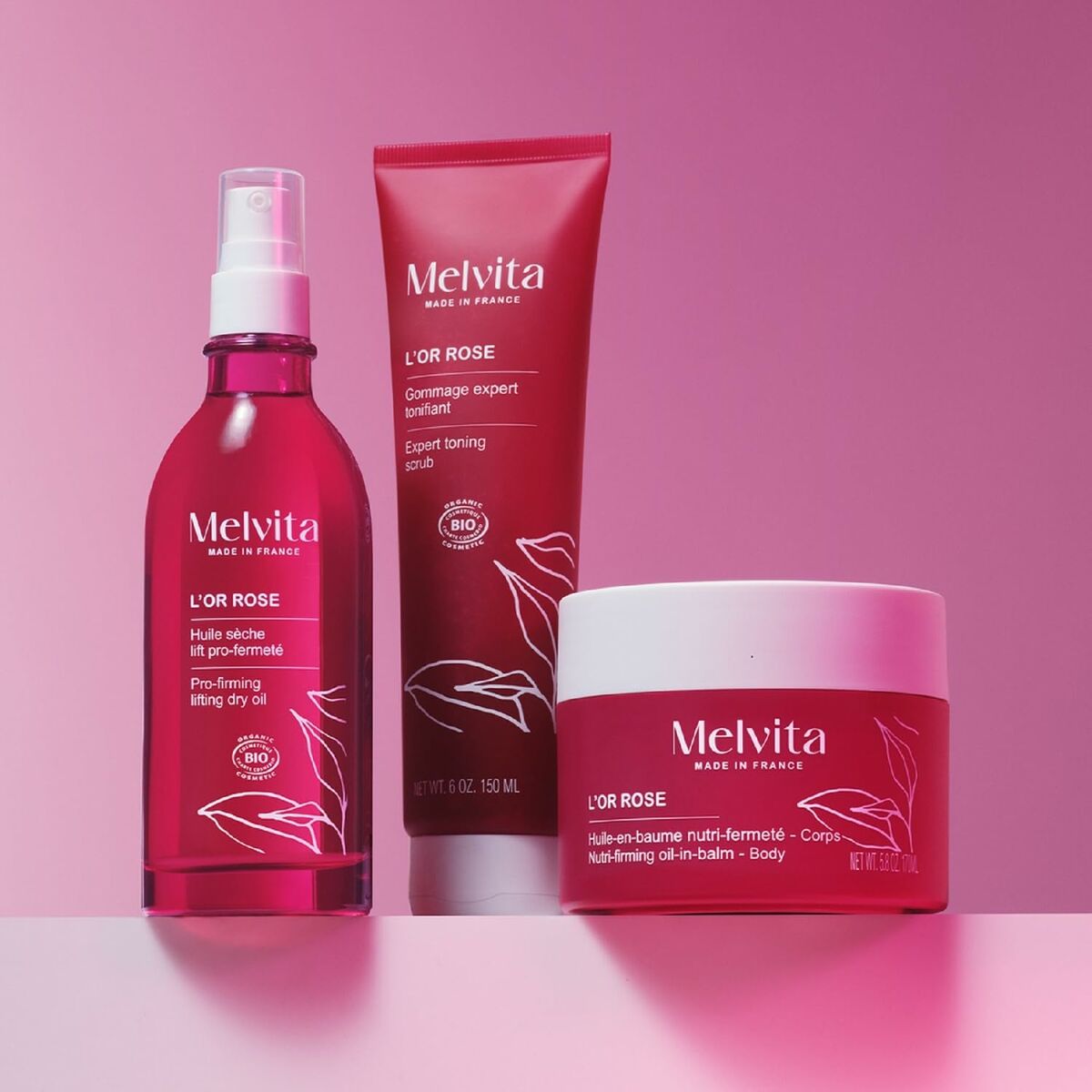 Melvita L'OR ROSE collection featuring body lotion, scrub, and dry oil in a vibrant pink setting.