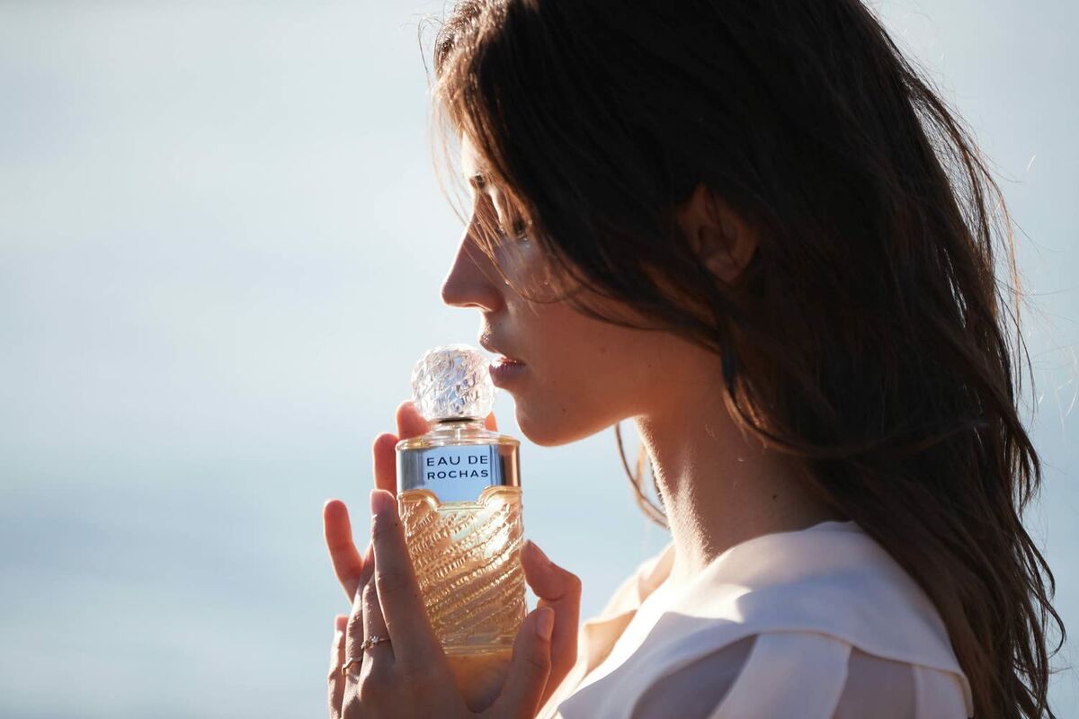 Woman holding Parfum Femme Rochas Eau de Rochas EDT near the shore, showcasing its elegant bottle.
