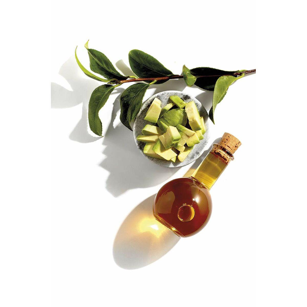 Cold-pressed oil with avocado pieces and green leaves on a white background for natural skincare.