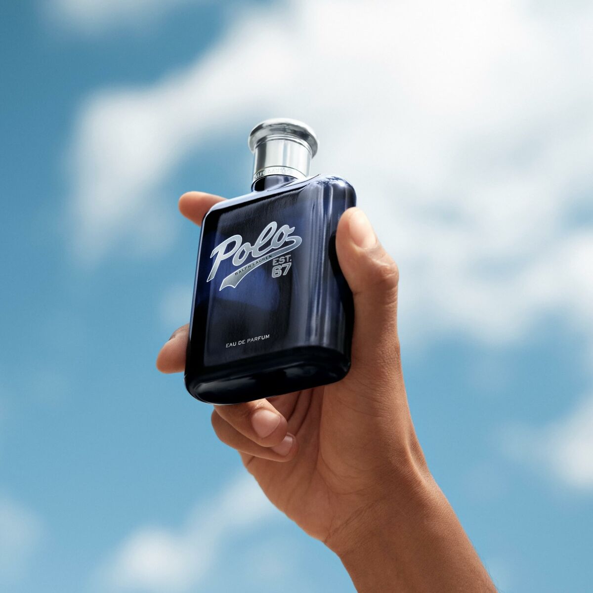 Bouteille de parfum homme Ralph Lauren POLO, tenue à la main, avec un ciel bleu en arrière-plan.