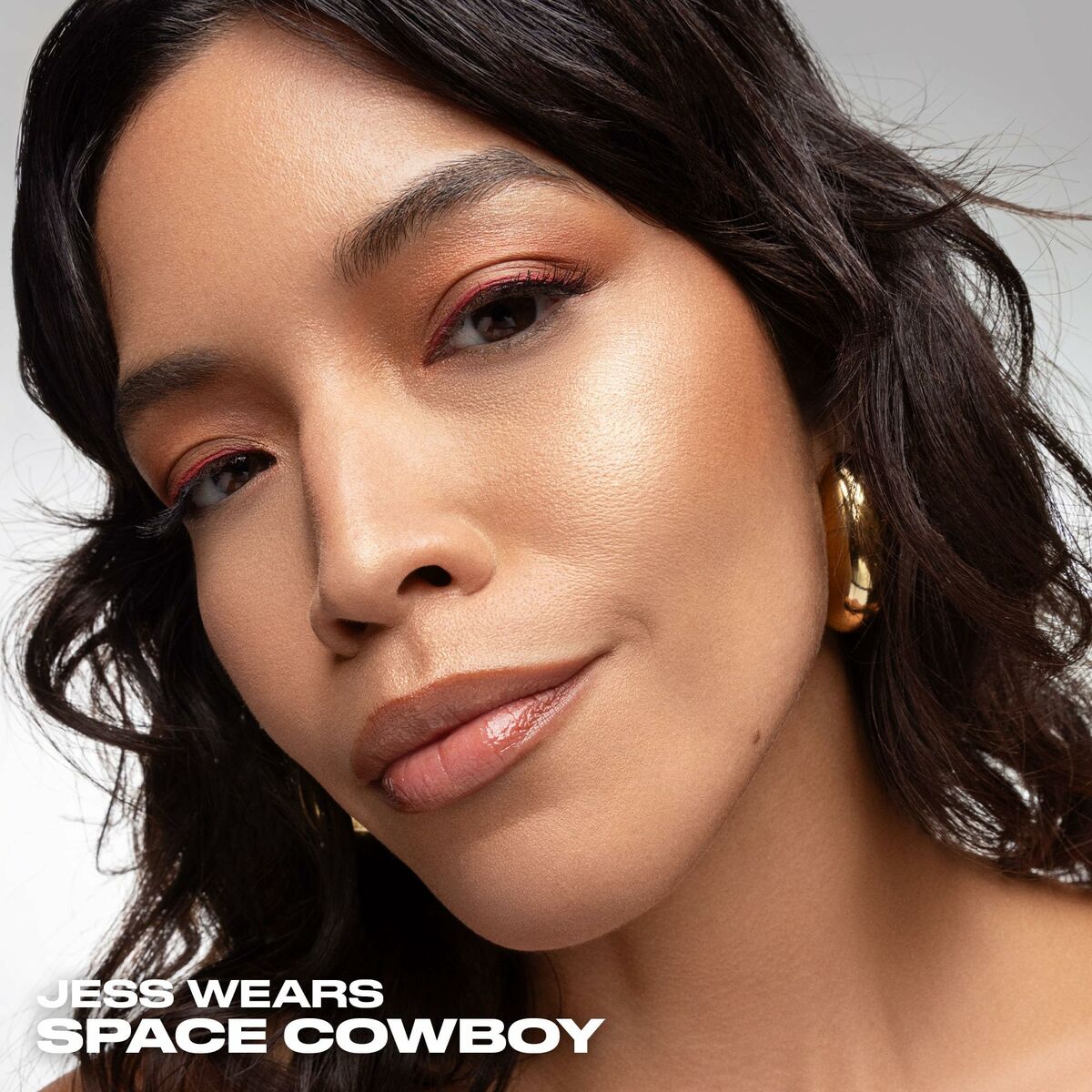 Close-up of a woman showcasing Urban Decay highlighter with a radiant makeup look.