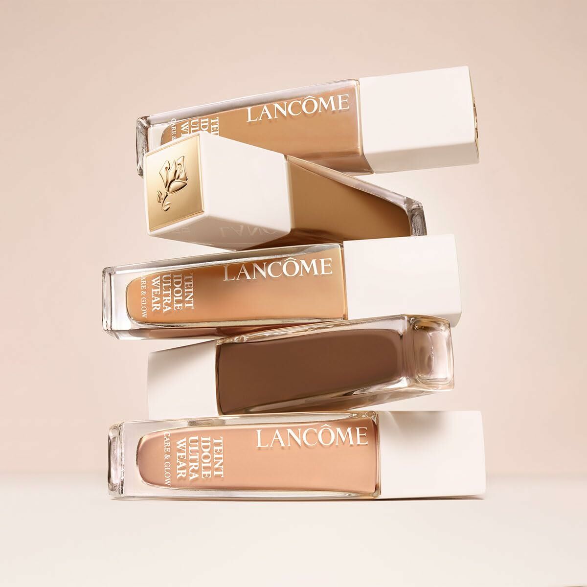 Flacon de base de maquillage liquide Lancôme Teint Idole Ultra Wear, teintes empilées sur fond clair.