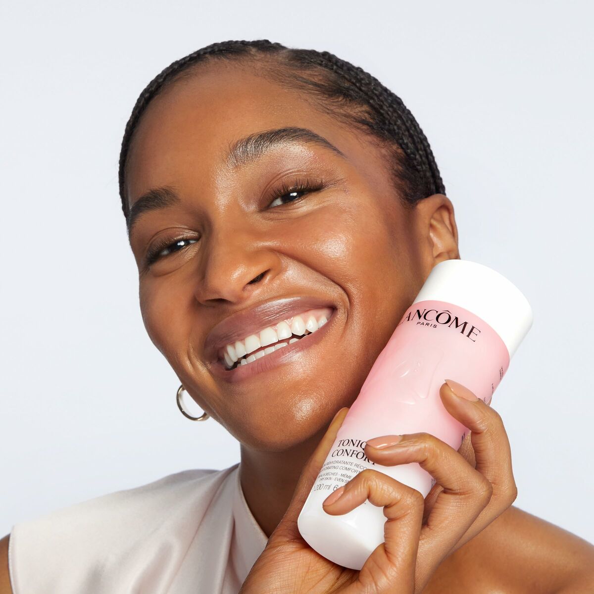 Femme souriante tenant le gel nettoyant visage Lancôme CONFORT 200 ml, idéal pour peau sèche.