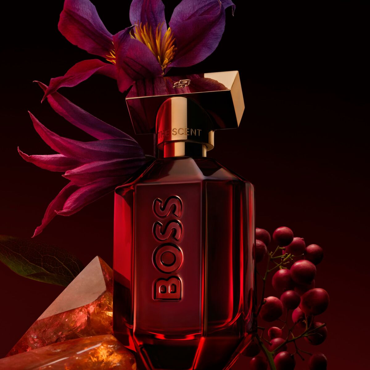 BOSS The Scent Elixir 30 ml perfume bottle surrounded by purple flowers and decorative stones.