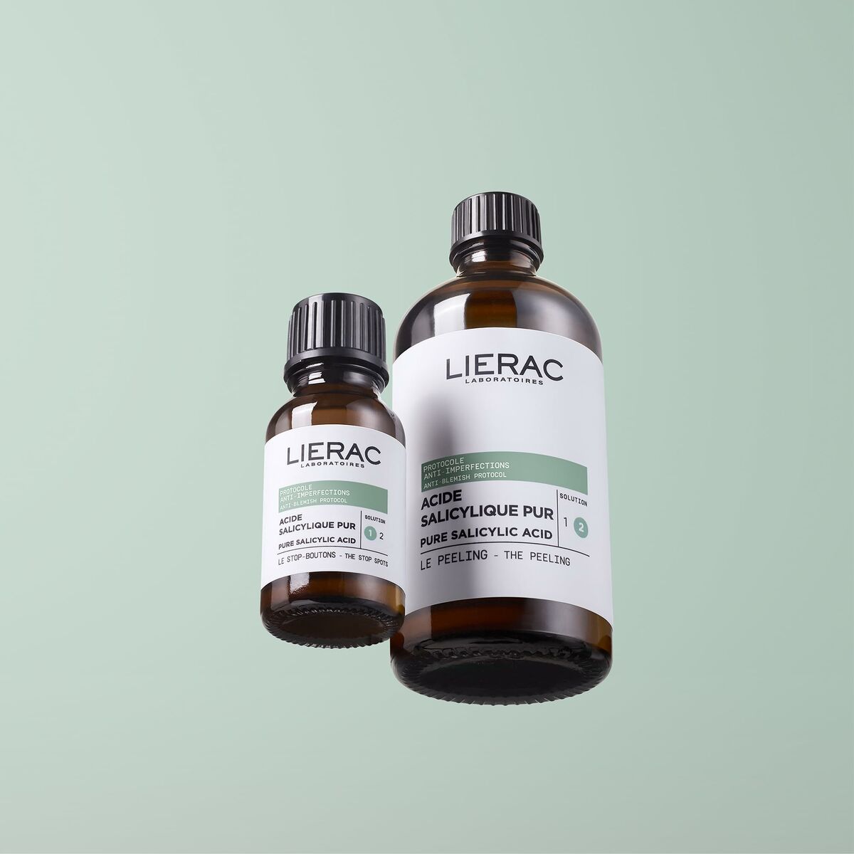 Lierac exfoliant visage with salicylic acid in two brown bottles against a green background.