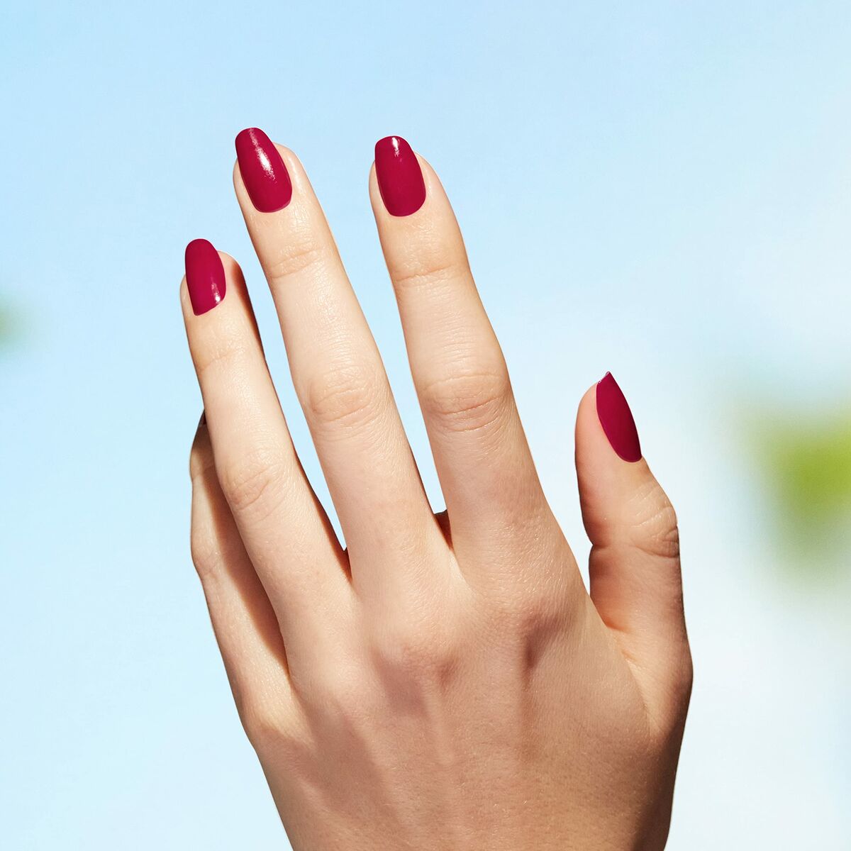 Mainly feminine hand with elegant red nail polish against a blue sky, showcasing beauty and craftsmanship.