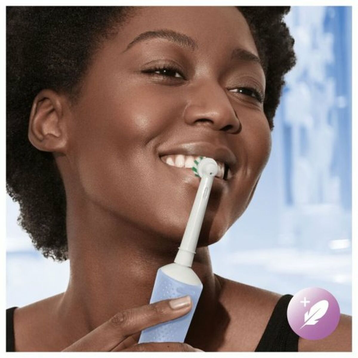 Person smiling while using a Braun electric toothbrush in blue and white for improved oral hygiene.