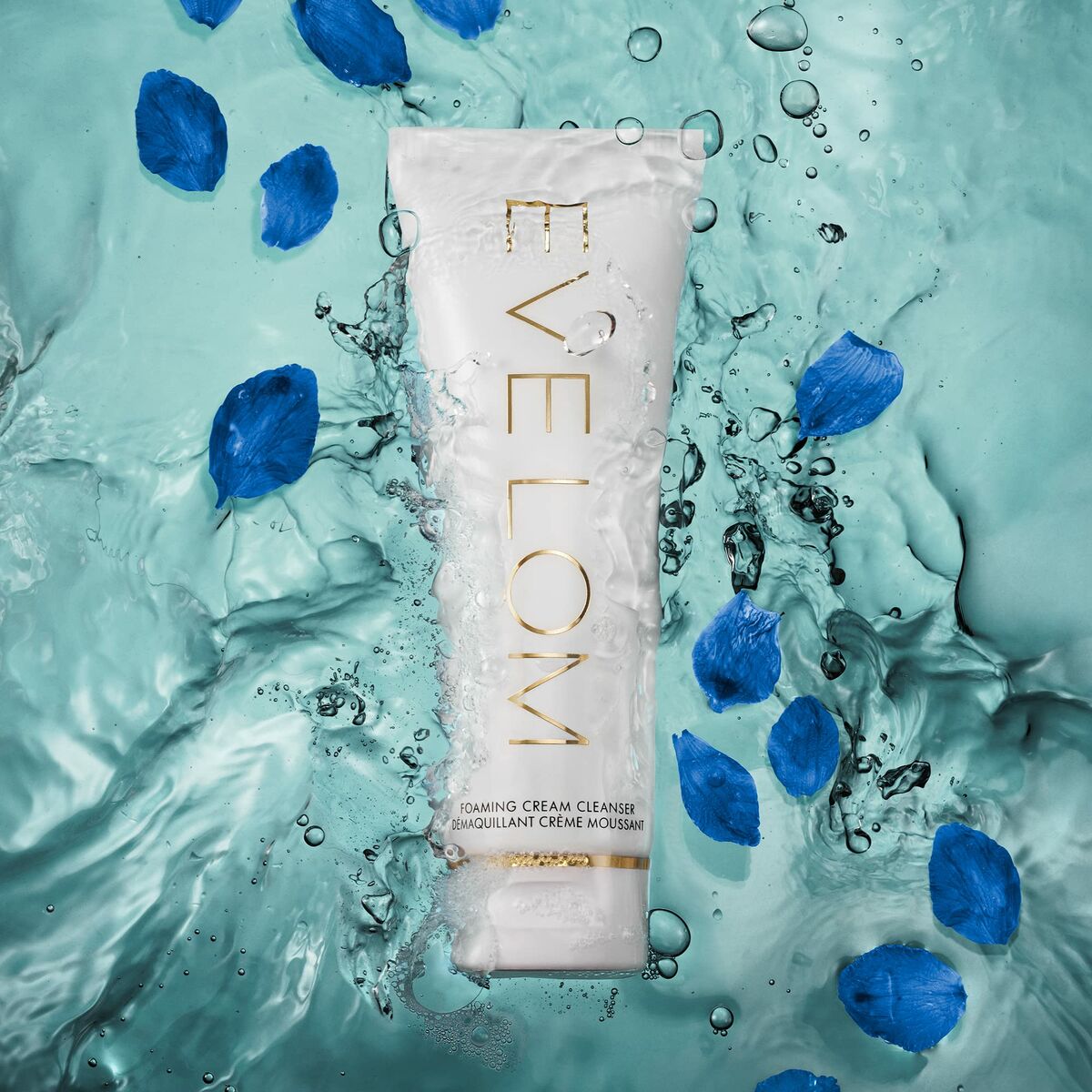 Eve Lom Mousse foaming cream cleanser displayed in water with blue petals, highlighting luxury skincare for radiant beauty.