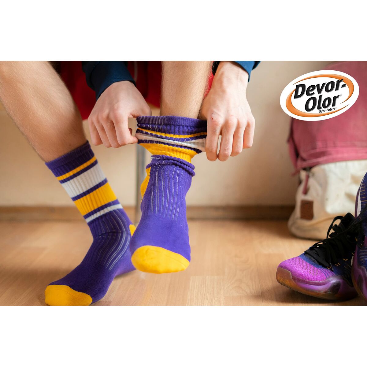 Person wearing colorful purple and striped socks, showcasing Devor-olor branding, on a wooden floor.