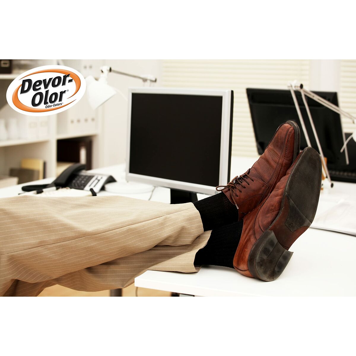 A pair of brown dress shoes on an office desk, showcasing a relaxed work environment with a computer in the background.