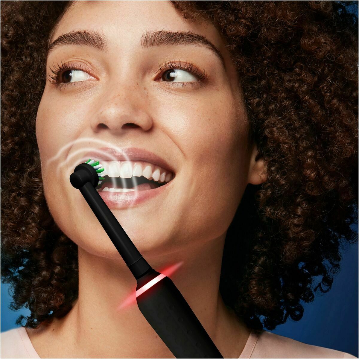 Femme utilisant une brosse à dents électrique Braun Noir, souriante, en train de se brosser les dents.