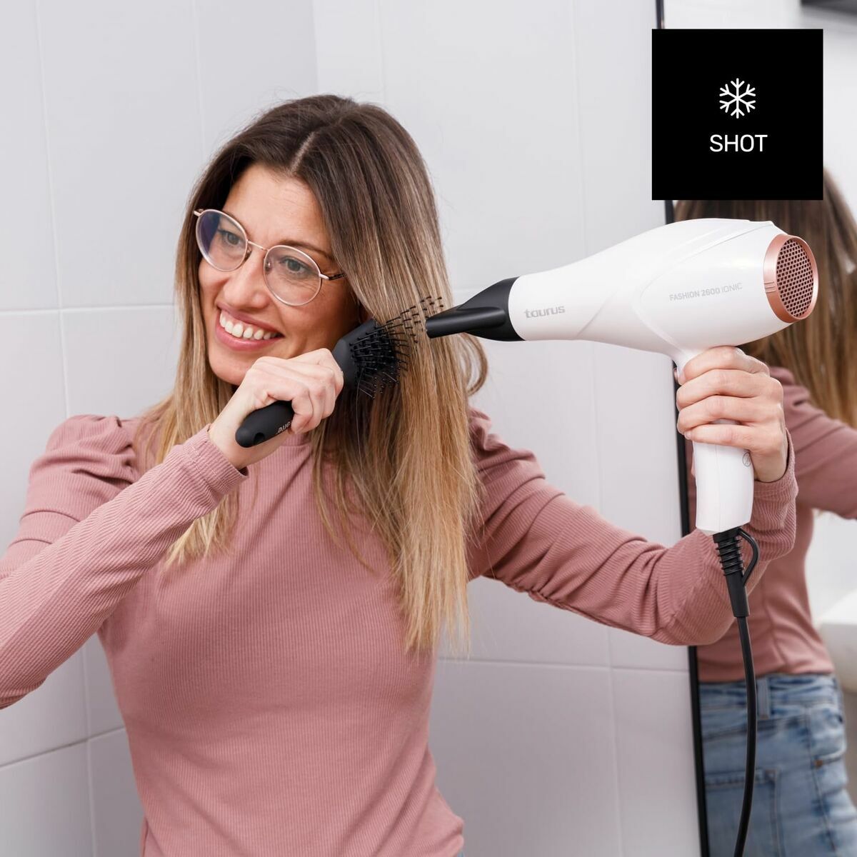 Woman using Taurus FASHION 2600 IO hairdryer while styling her hair in a bathroom.