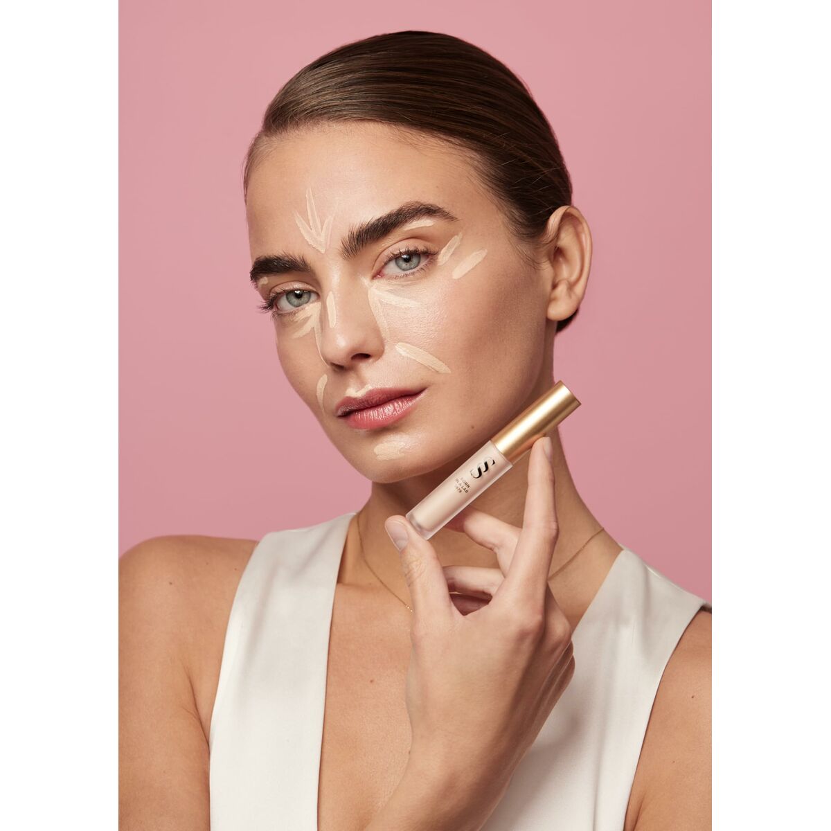 Modèle appliquant le sérum Éclaircissant Sensilis SKIN GLOW FACIAL sur son visage, avec fond rose.