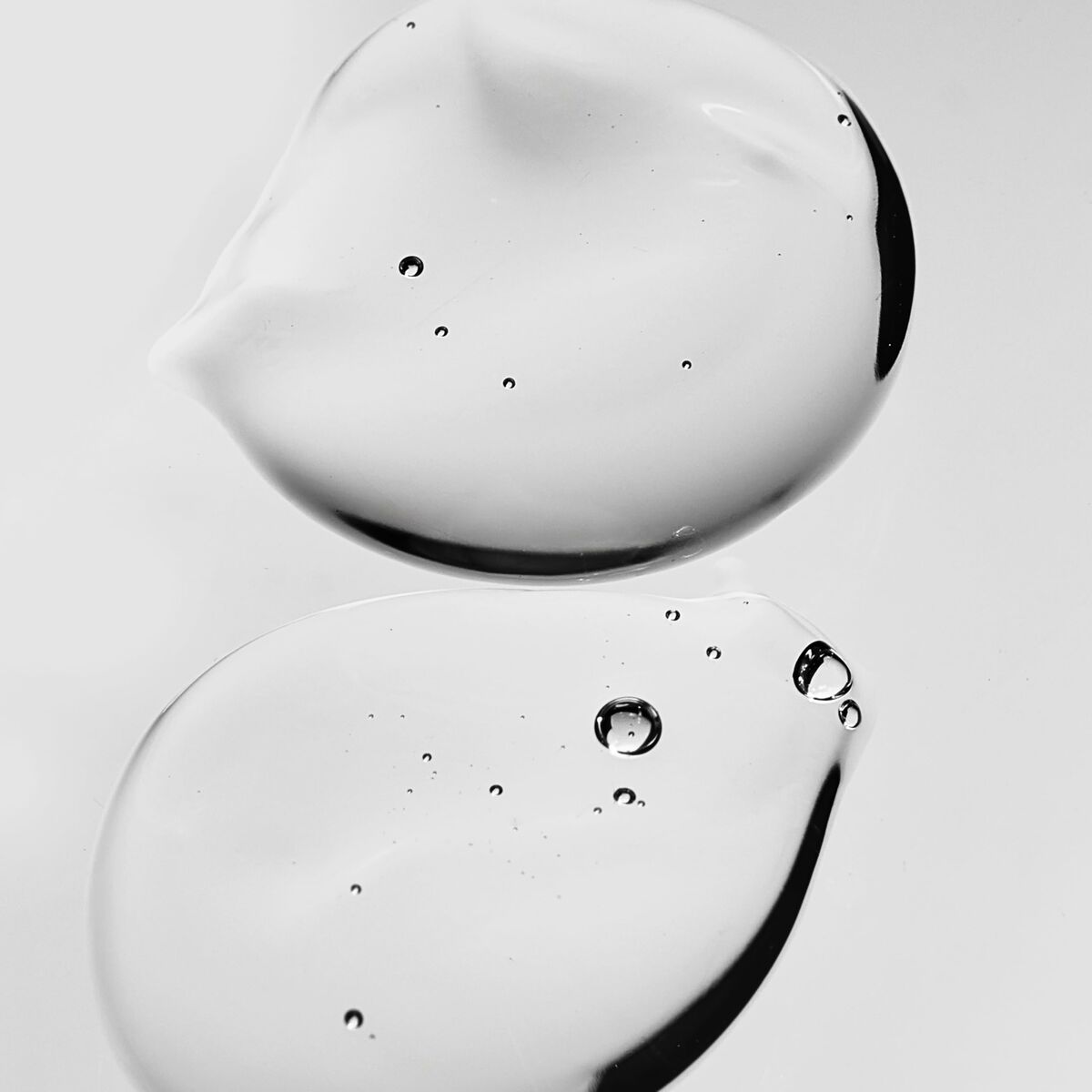 Transparent gel drops on a reflective surface, showcasing a clean aesthetic for skincare products.