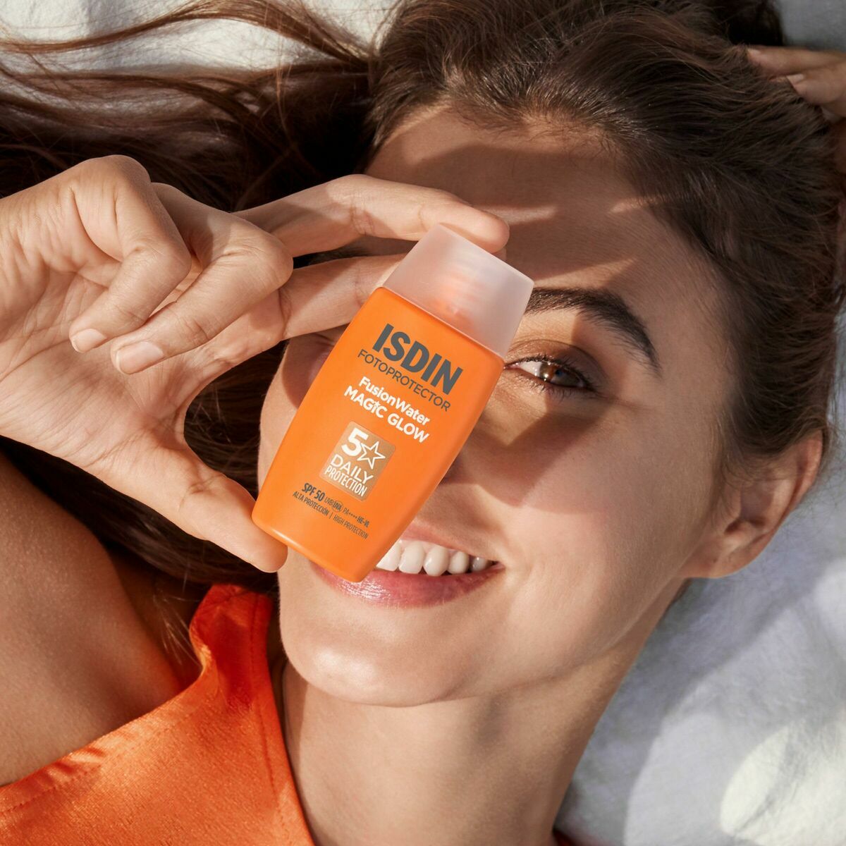 Femme souriante tenant le Protecteur Solaire Isdin FOTOPROTECTORES ISDIN Magic Glow en extérieur.