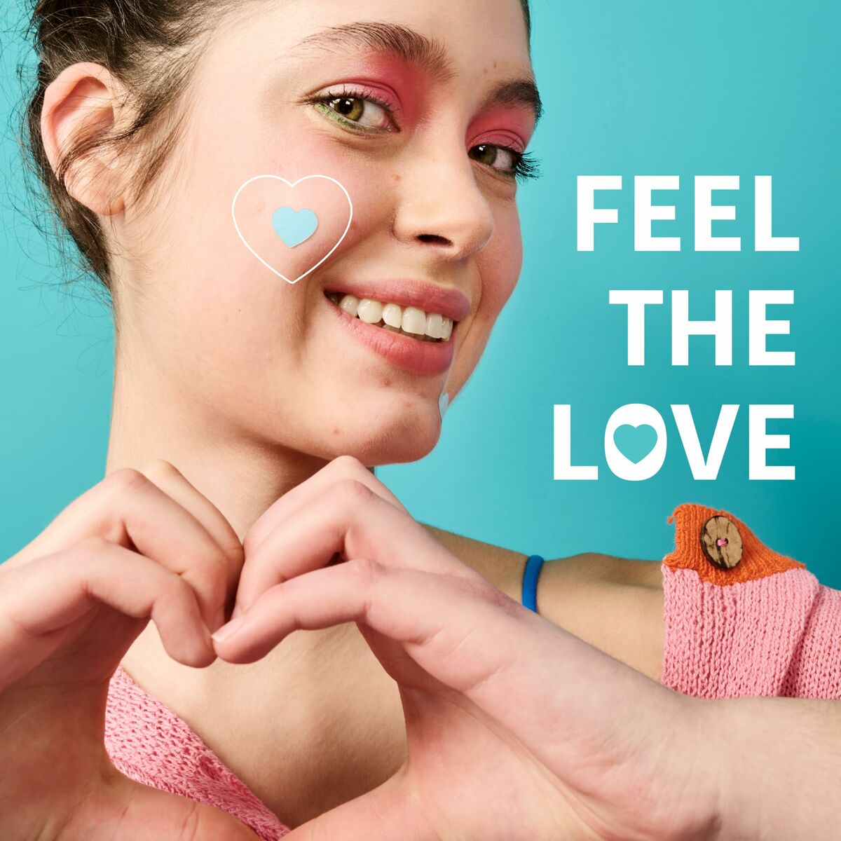 Young woman smiling with heart design on cheek, expressing joy and love, vibrant background, wearing a pink top.