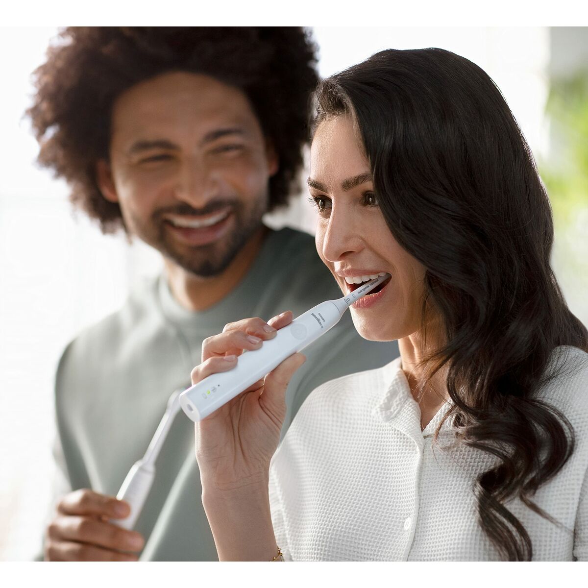 Une femme se brosse les dents avec la brosse à dents électrique Philips HX3651/13, blanche, pendant qu'un homme sourit.
