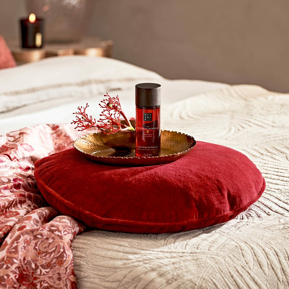 Protecteur solaire Rituals sur coussin rouge décoratif dans un environnement apaisant.