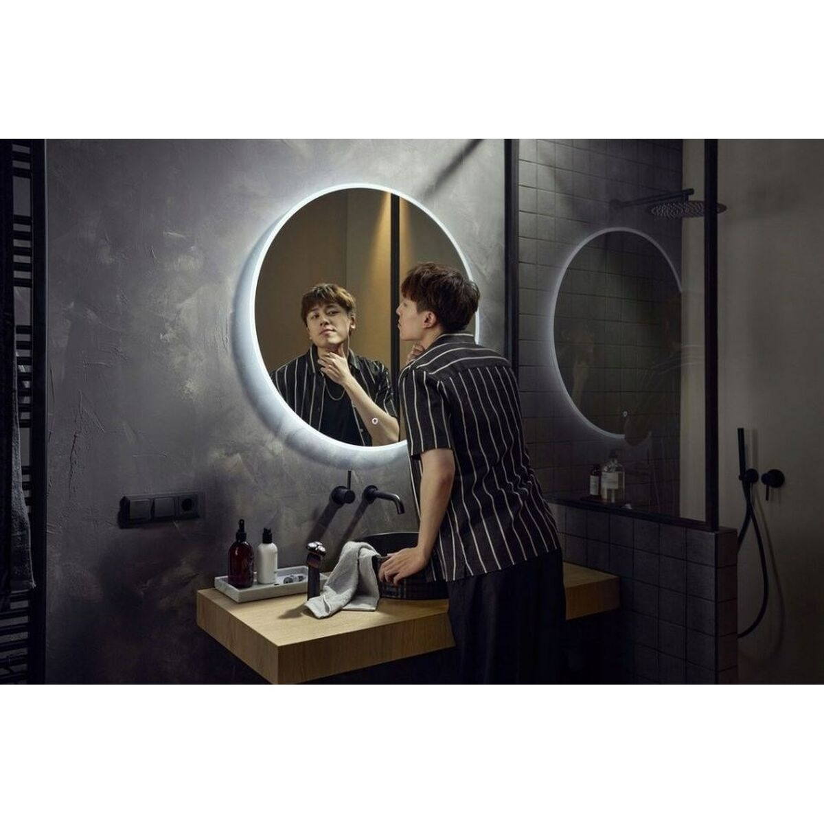 Young man grooming in a modern bathroom with circular mirror and stylish vanity.